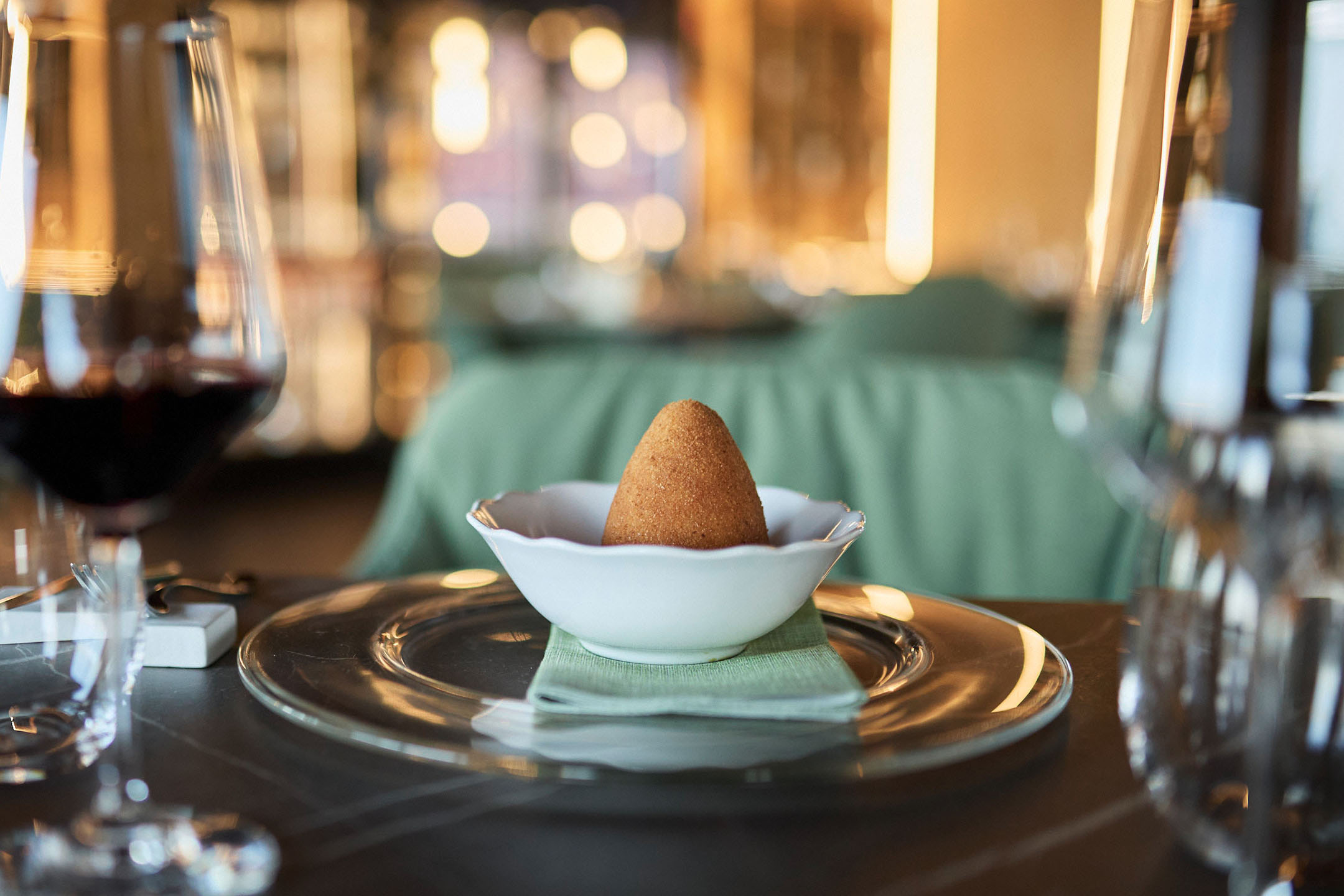 Zelta arancini baltā bļodā uz eleganta restorāna galda.