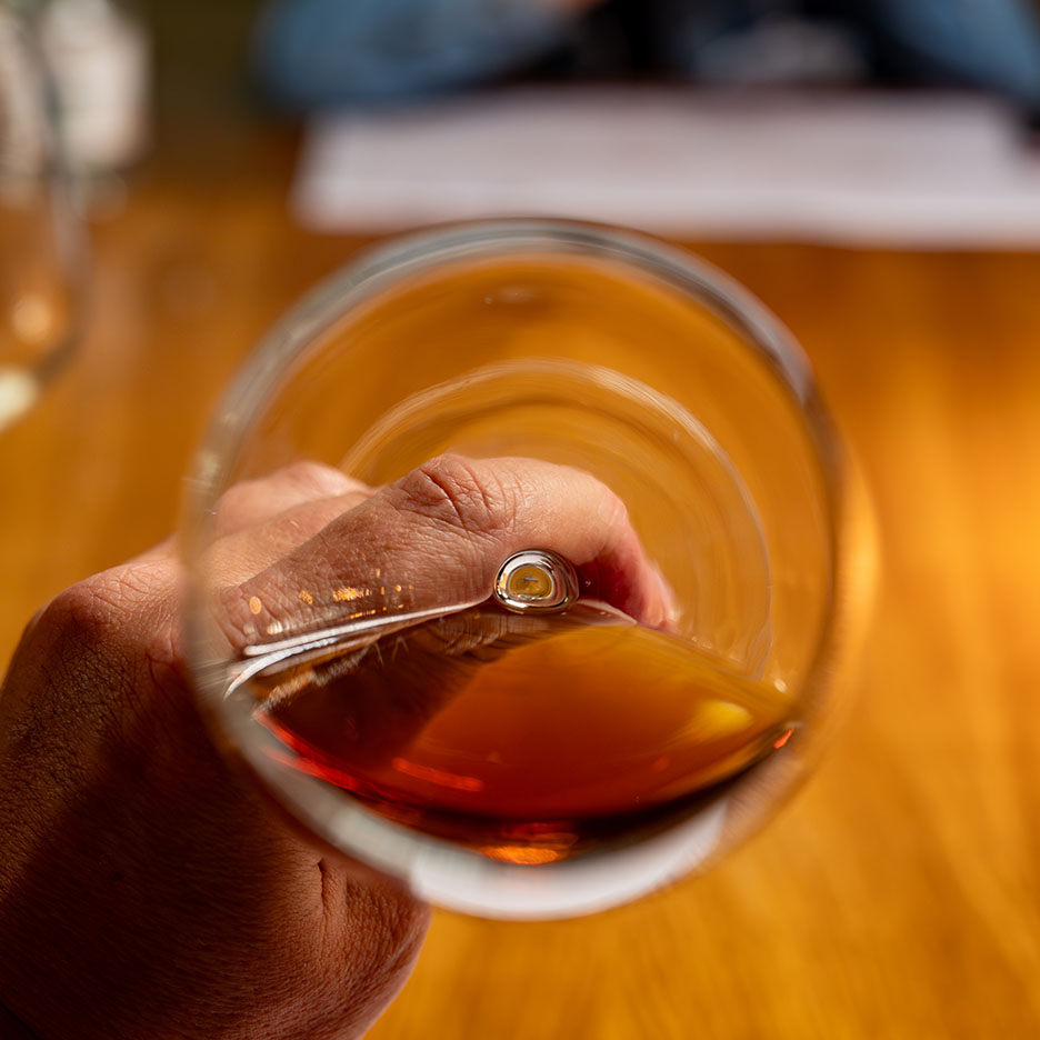 Roka tur sarkanvīna vai dzintarkrāsas stiprā alkohola glāzi uz koka galda.