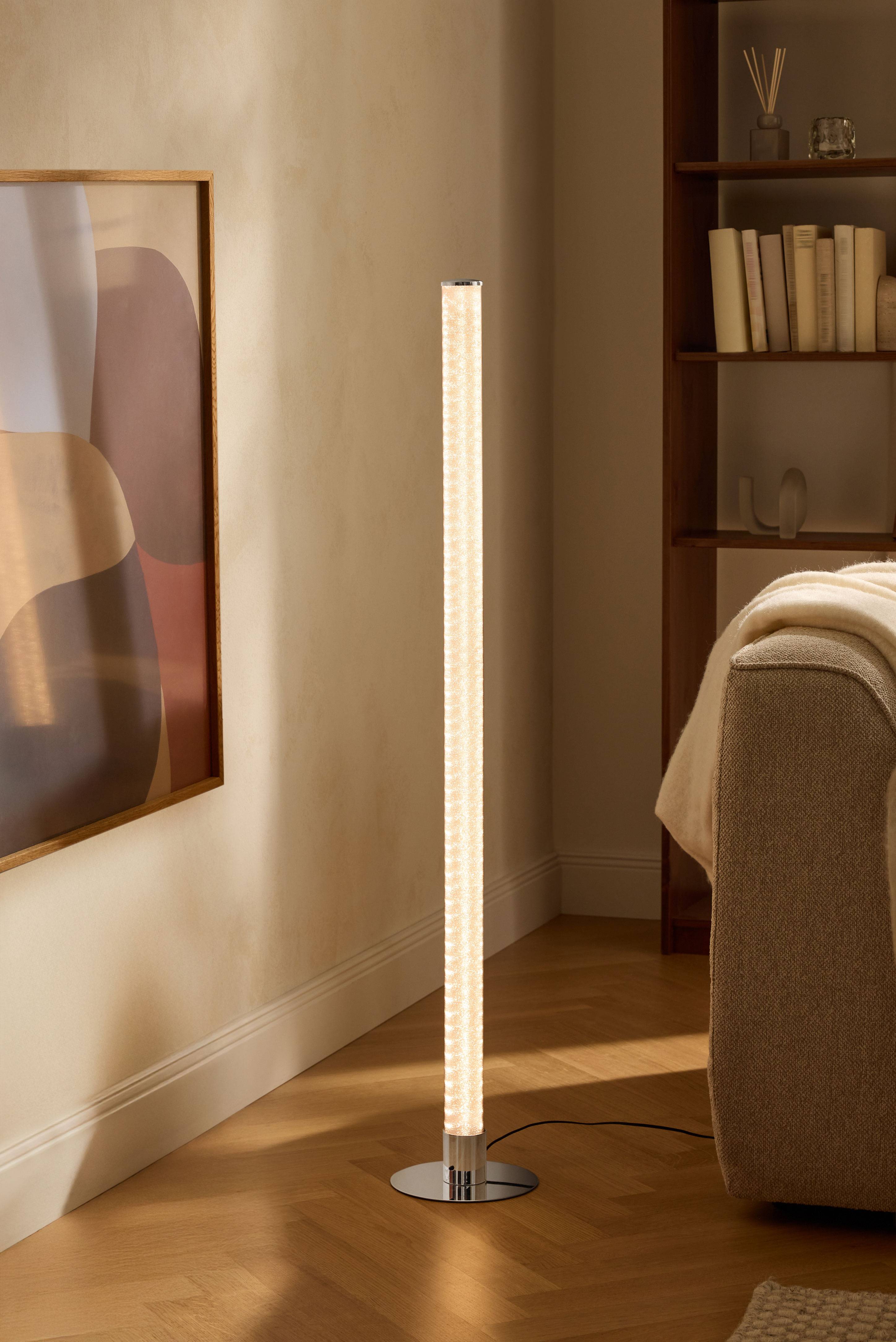 Mūsdienīga stāvlampa viesistabā ar grāmatu plauktu un dīvānu.