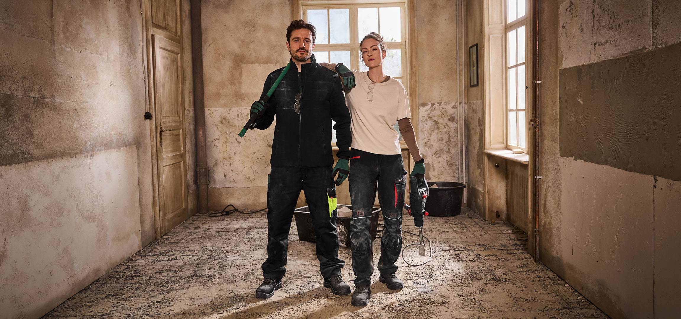 Divi celtnieki darba apģērbā ar instrumentiem būvlaukumā.