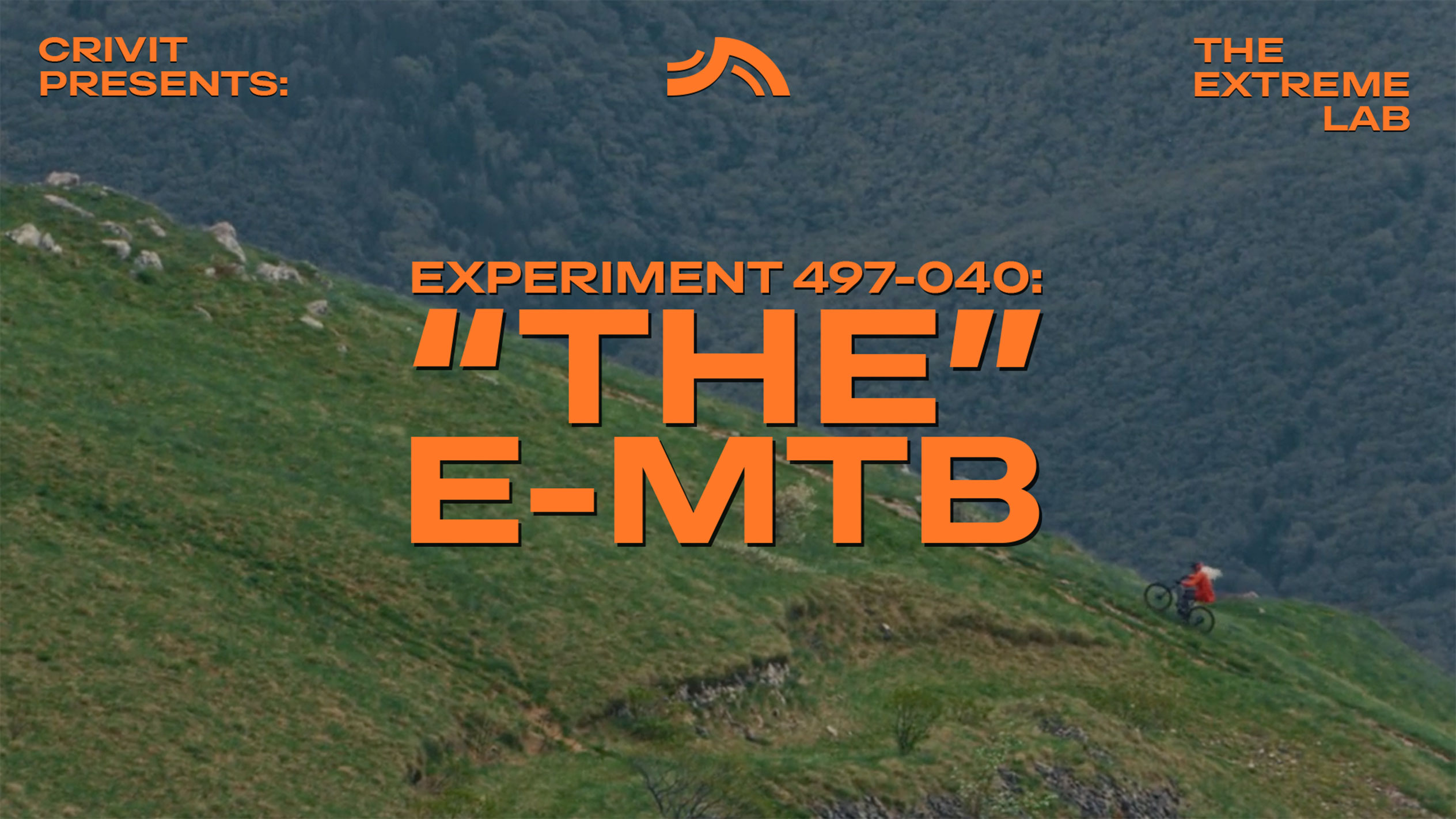 Kalnu riteņbraucējs uz zāļainas nogāzes, ar tekstu 'THE E-MTB' un 'THE EXTREME LAB'.