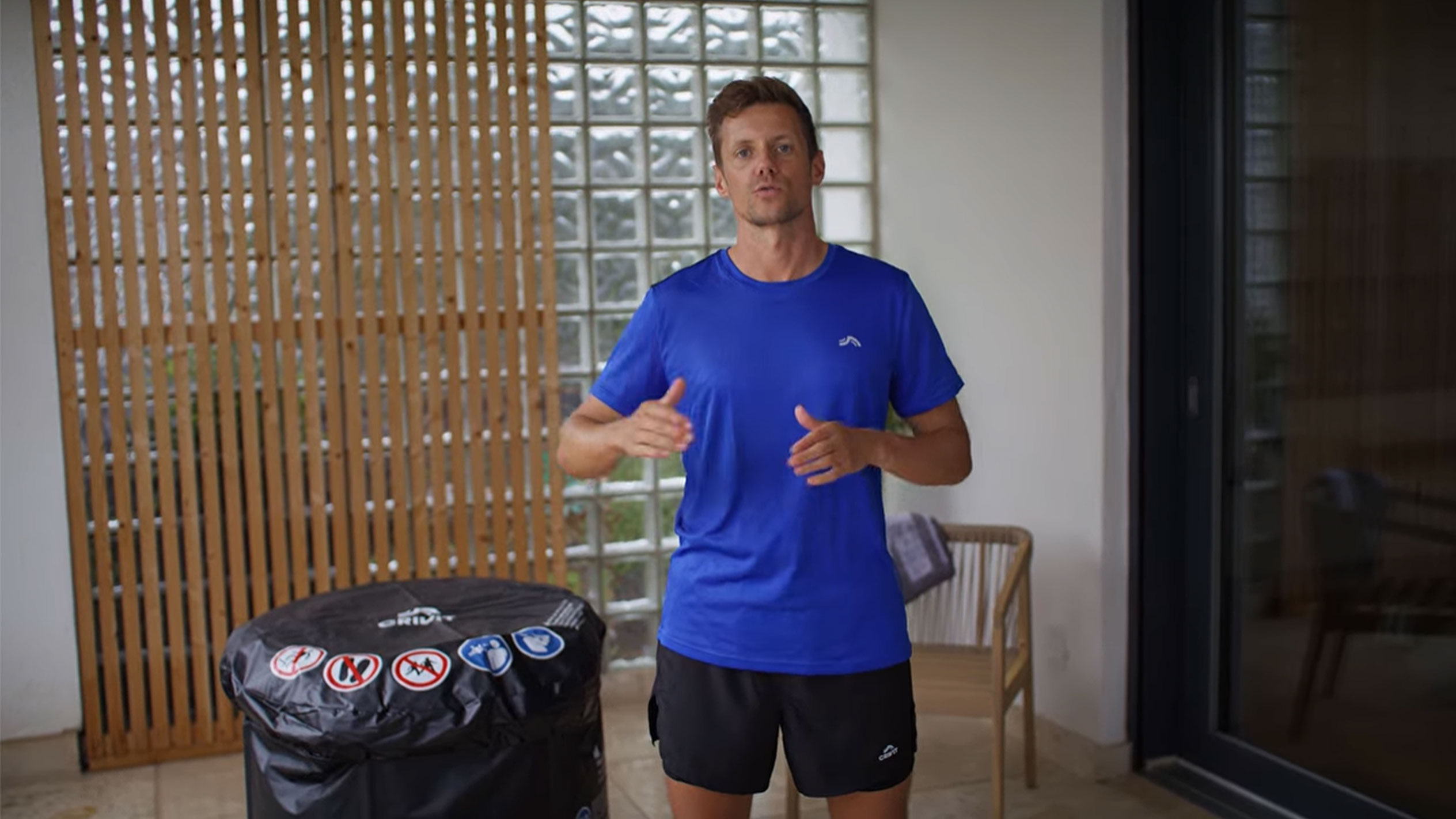 Мужчина в синей футболке и черных шортах, рядом с черным чехлом для джакузи.
