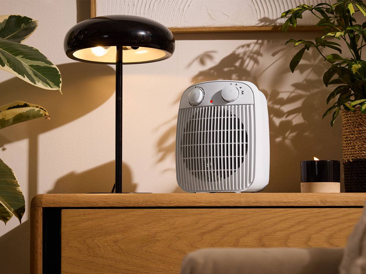 Белый обогреватель и черная настольная лампа на деревянной мебели в уютной комнате.