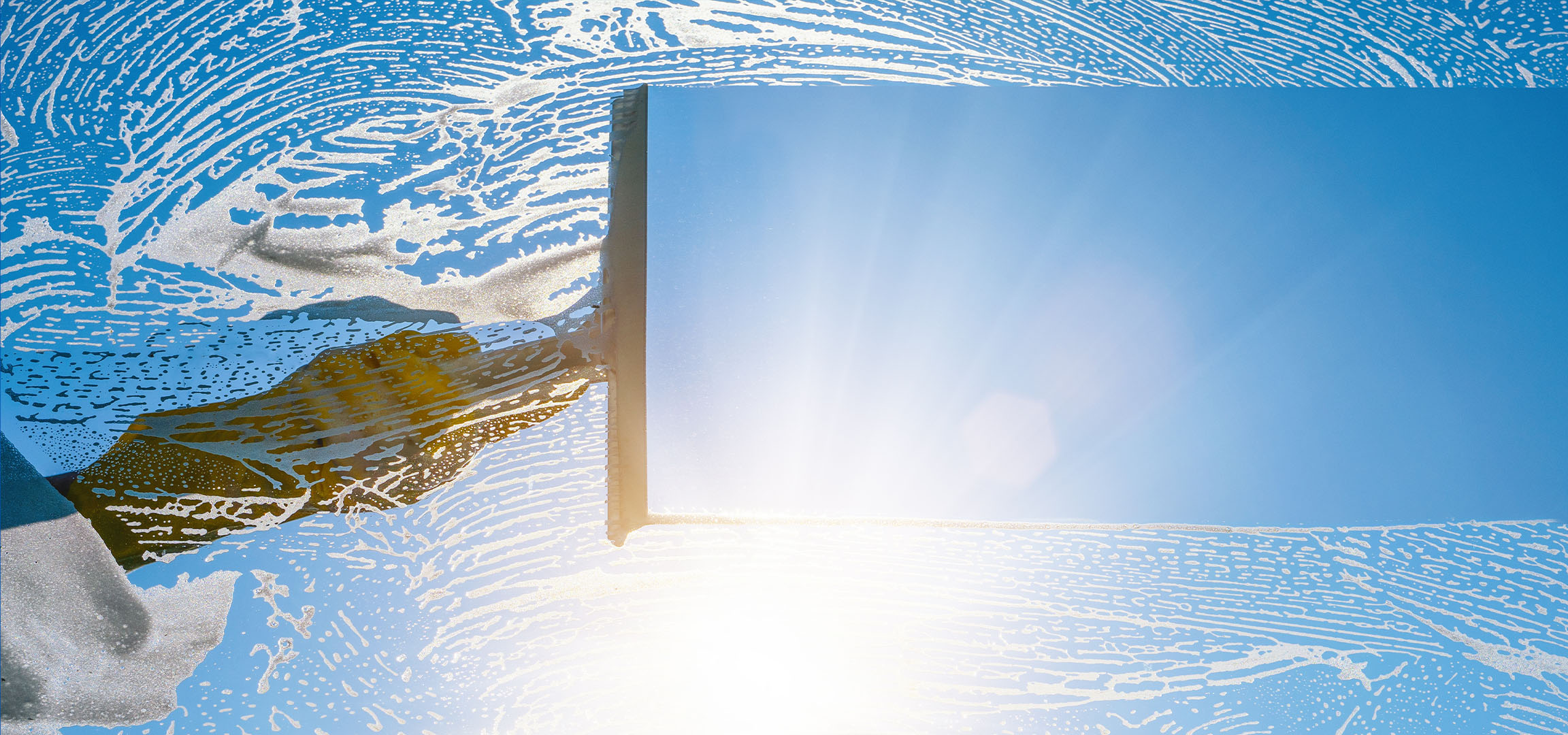 Мытье окон с мыльной пеной на фоне голубого неба.