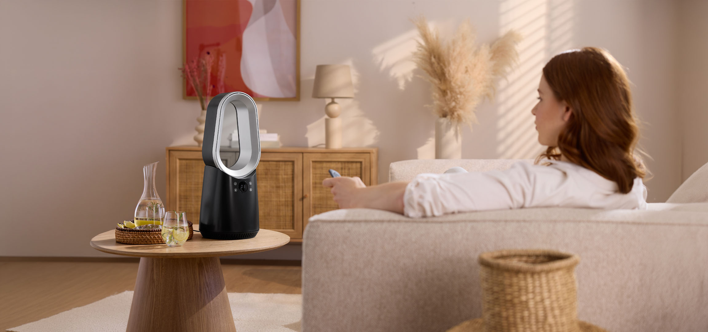 Женщина на диване с пультом, современный вентилятор и напитки на столе.