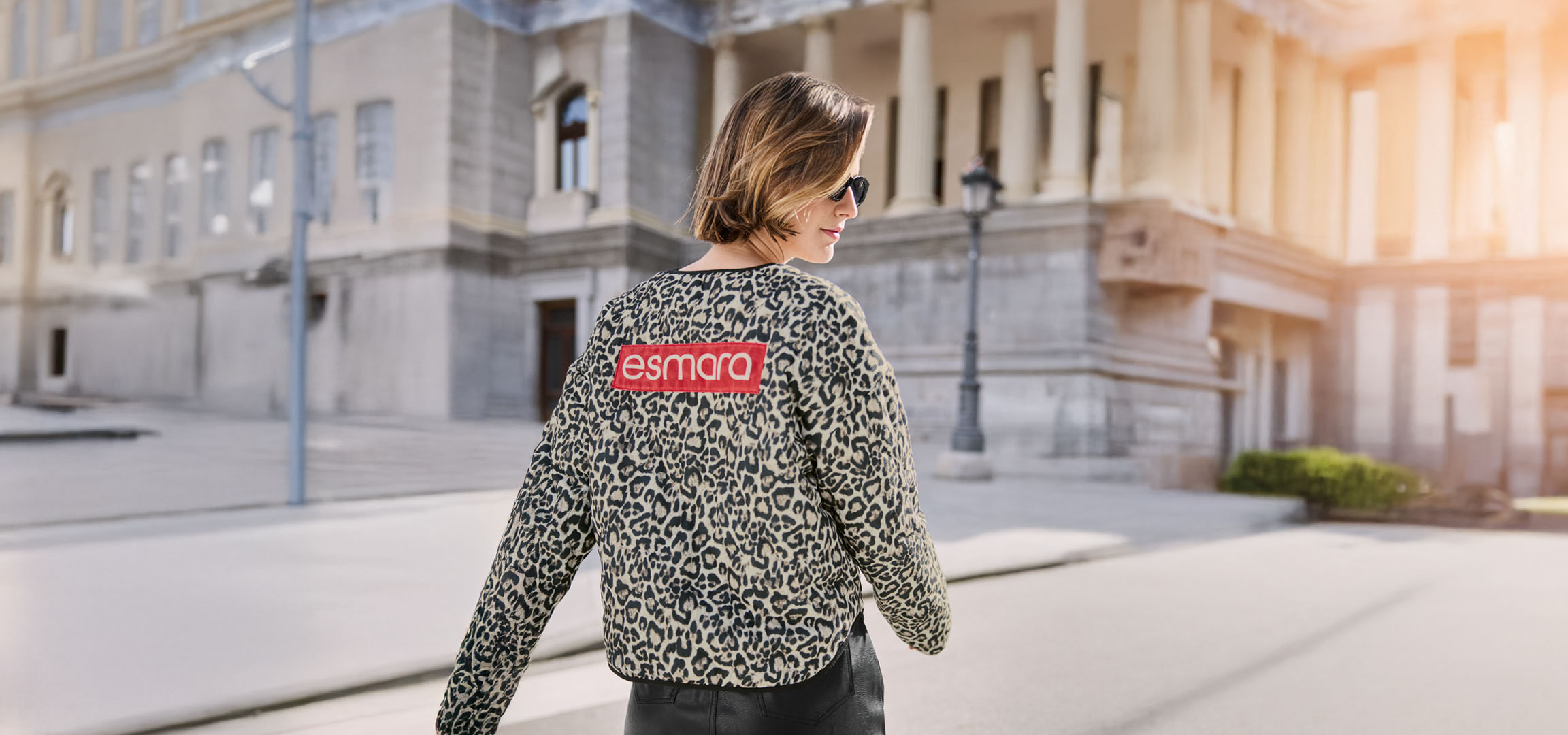 Женщина в леопардовой куртке Esmara, солнцезащитных очках, на городской улице.