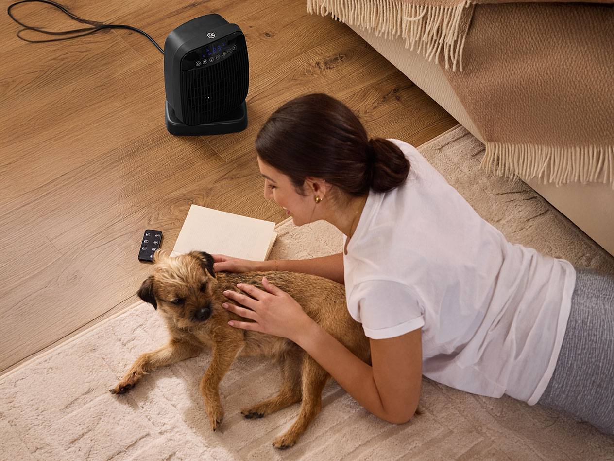 Женщина гладит собаку рядом с черным обогревателем на полу.