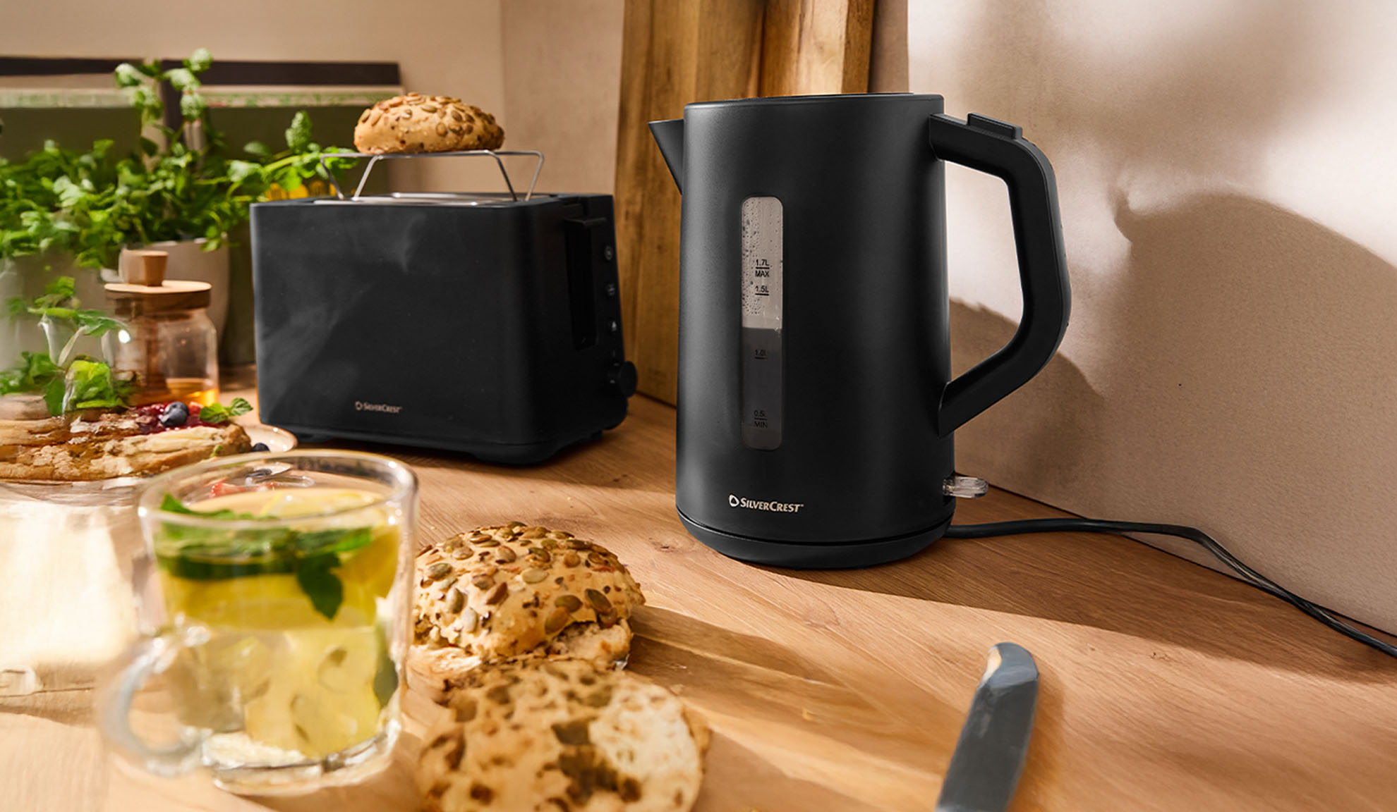 Черный чайник и тостер SilverCrest на деревянном столе с завтраком.