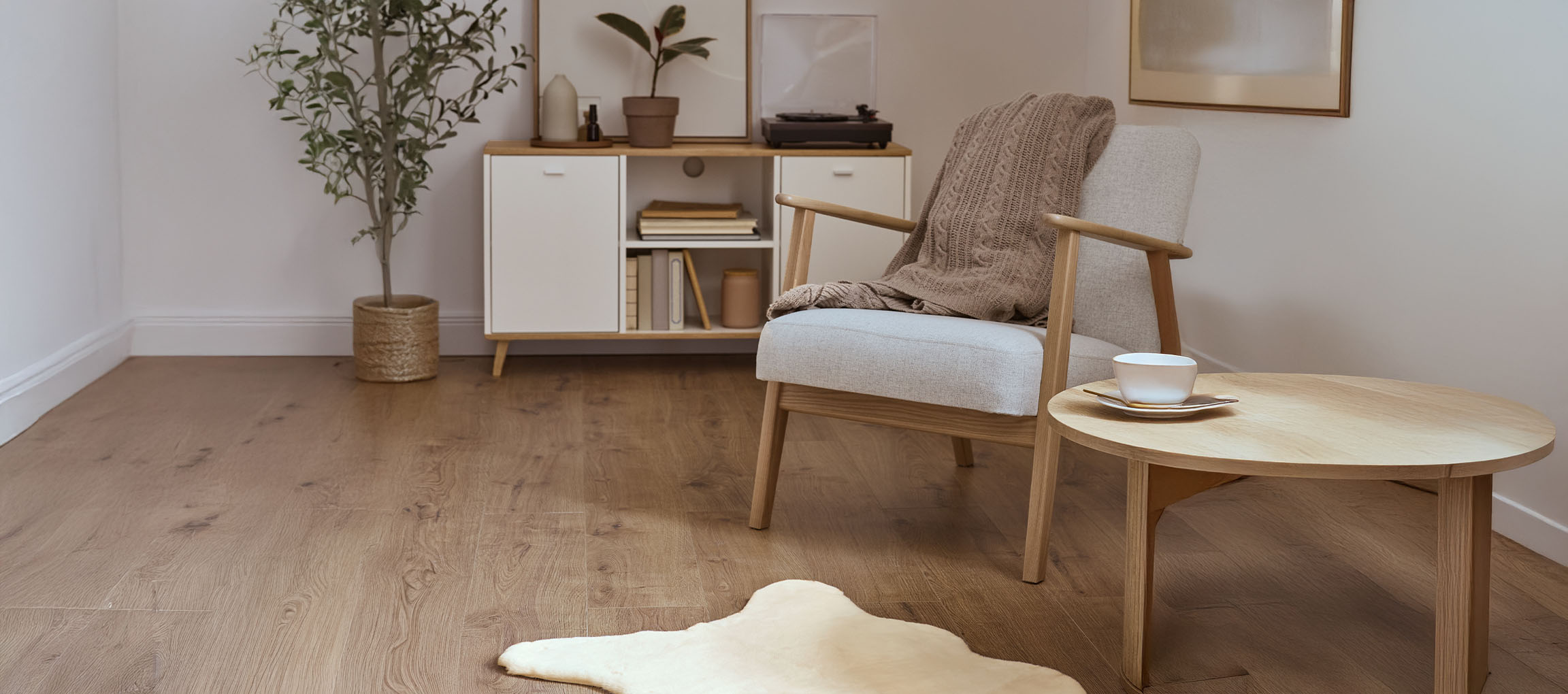 Pelēks auduma atzveltnes krēsls ar adītu pledu, koka kafijas galdiņš un moderna bufete.