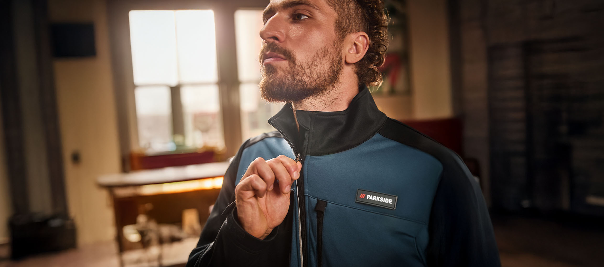 Vīrietis zili melnā Parkside darba jakā aizver rāvējslēdzēju