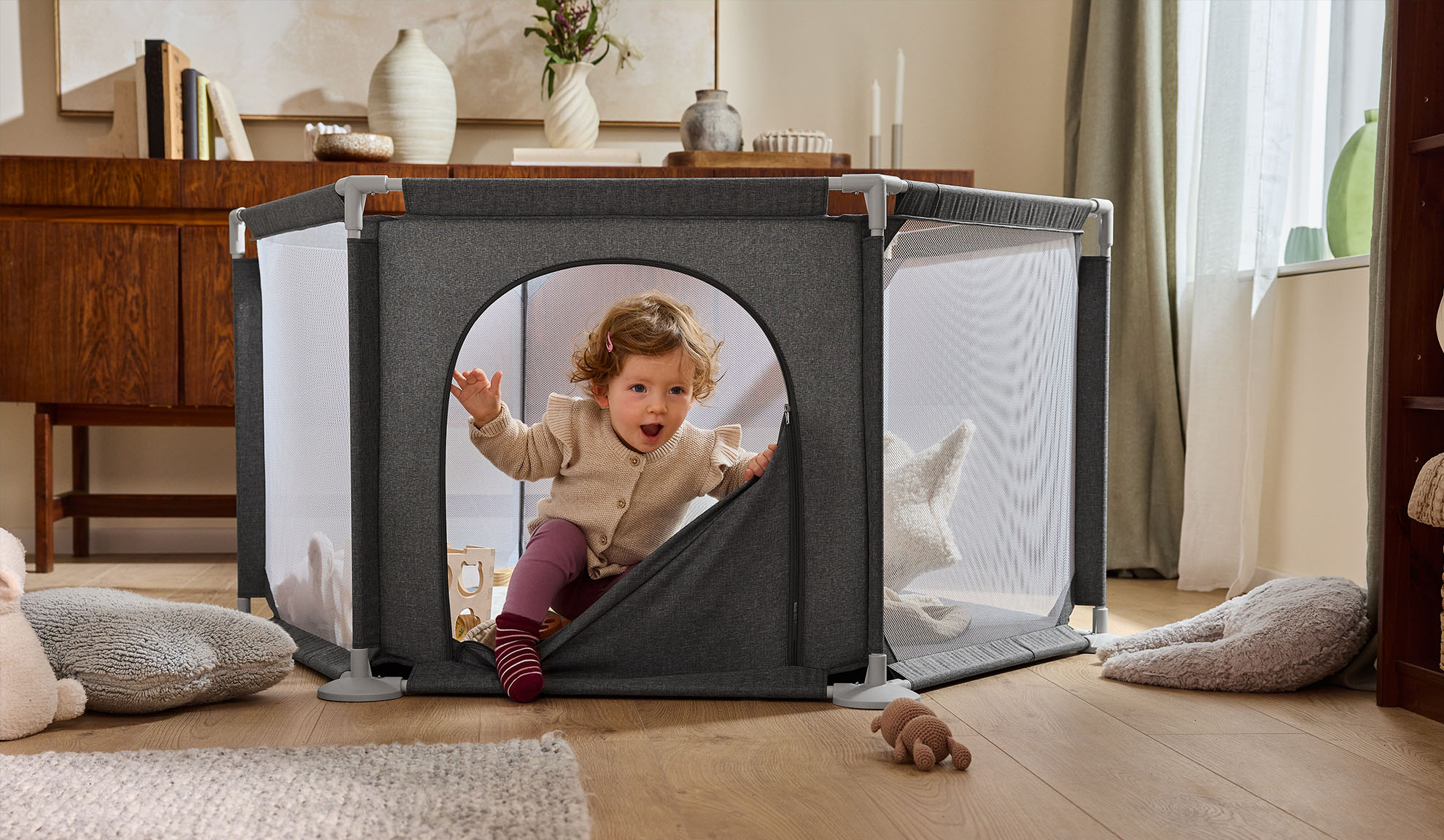 Priecīgs mazulis rāpo ārā no pelēka manēžas mājīgā viesistabā.