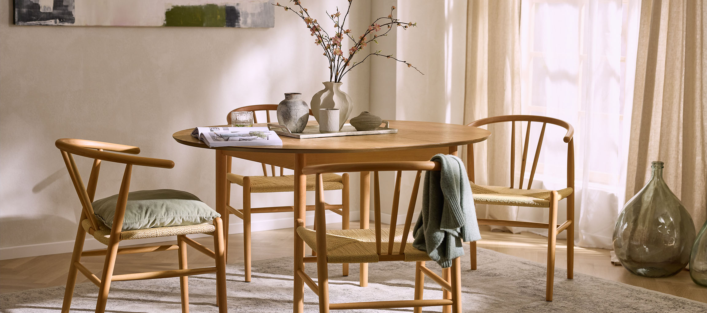 Ēdamistaba ar apaļu koka galdu, koka krēsliem ar virvju sēdekļiem un dekoratīvām vāzēm.