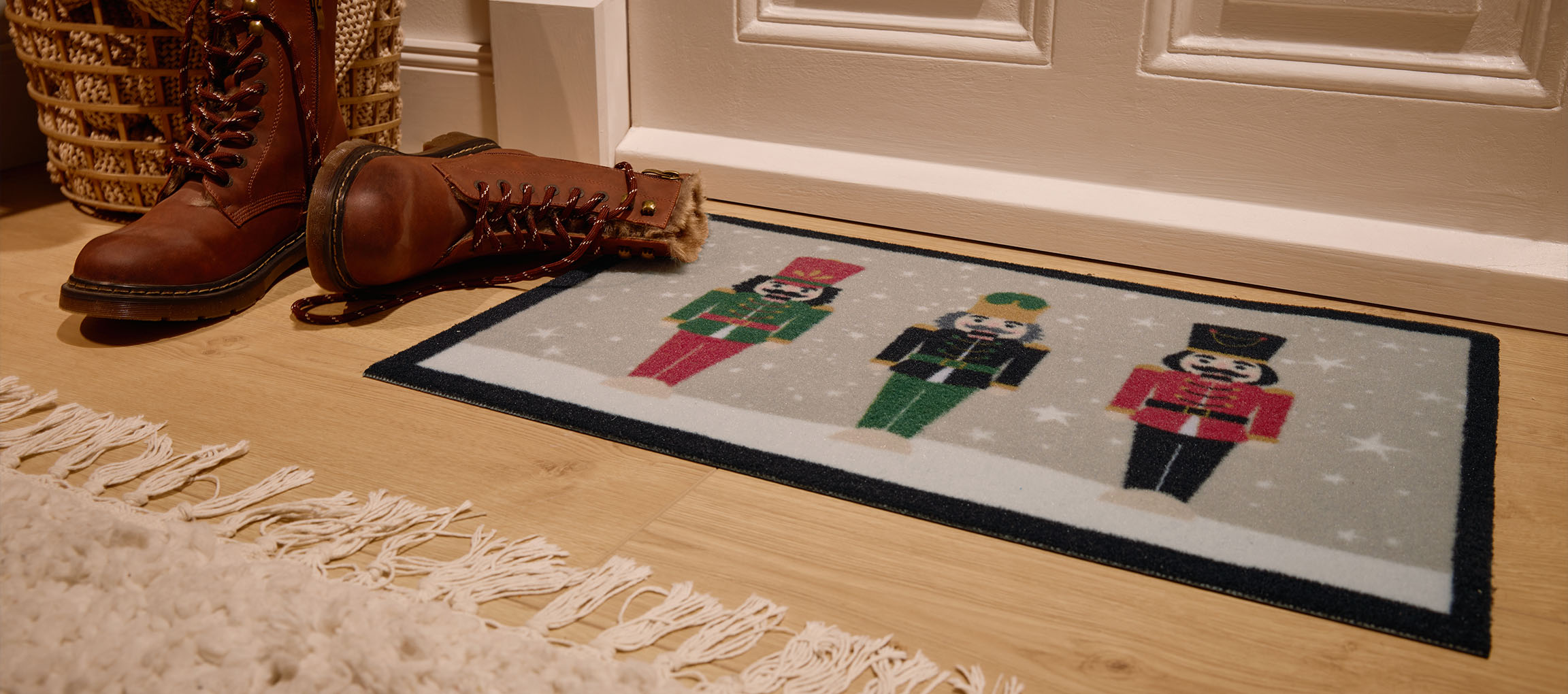 Рождественский коврик с щелкунчиками, коричневые ботинки и плетеная корзина у входа.
