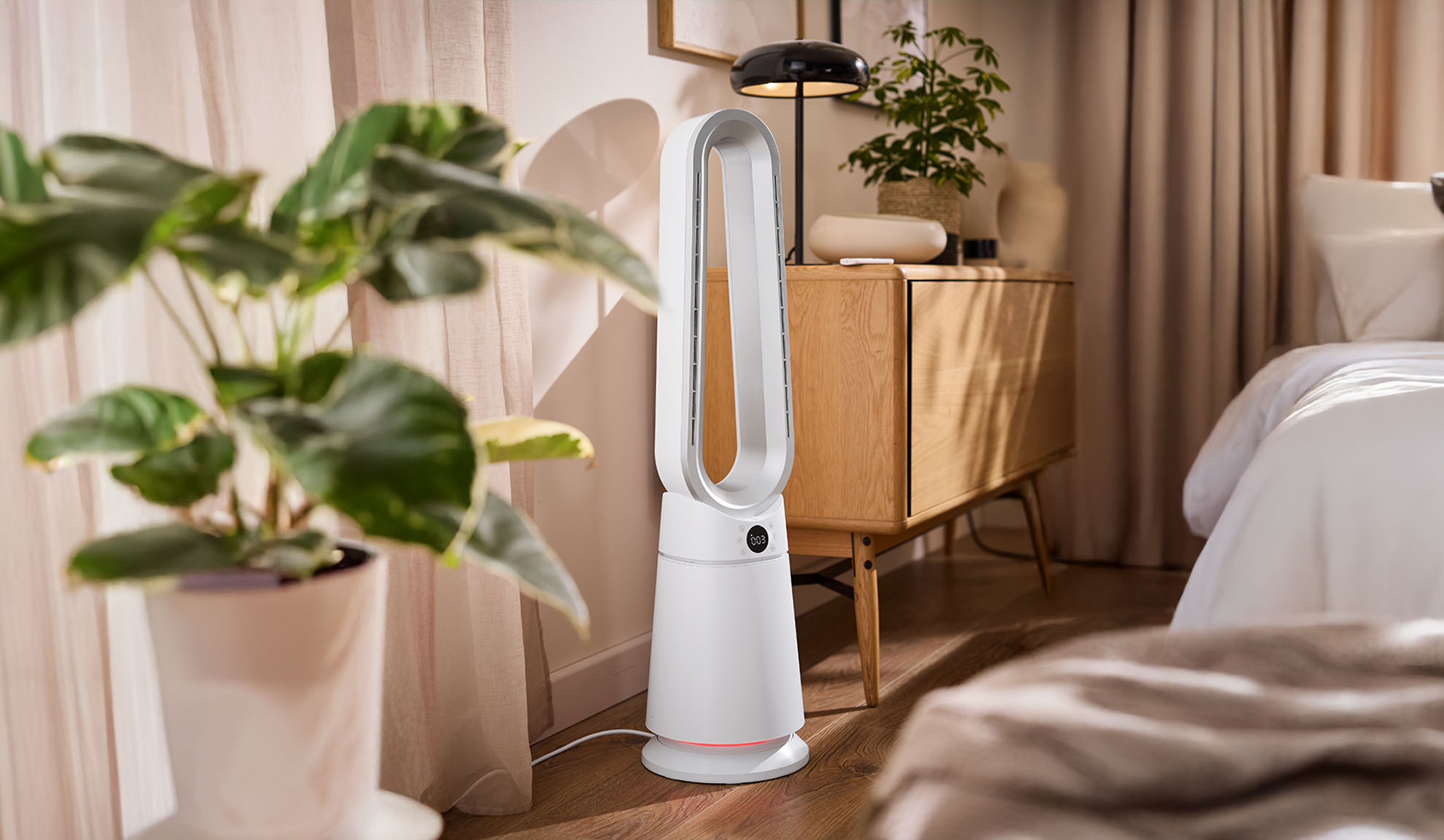 Balts torņa ventilators modernā guļamistabā ar augiem un koka mēbelēm.