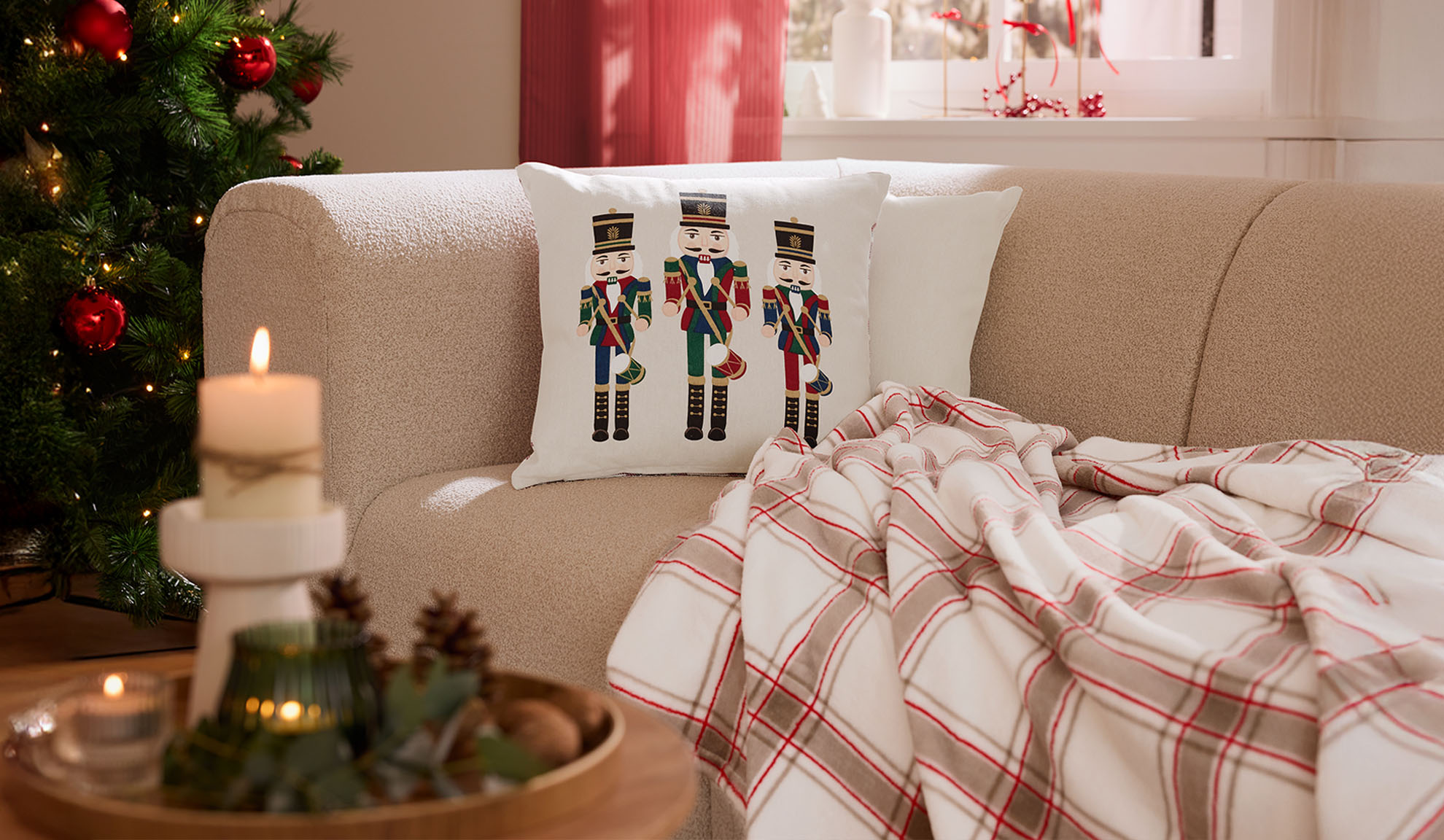 Ziemassvētku viesistaba ar dīvānu, riekstkožu spilveniem, rūtainu pledu un svecēm.