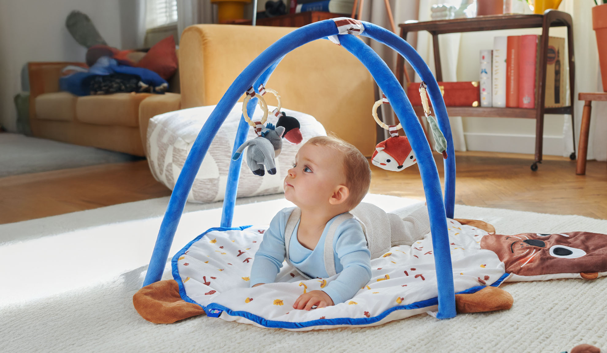 Ребенок играет на игровом коврике Tiny Love с аркой в форме животных.