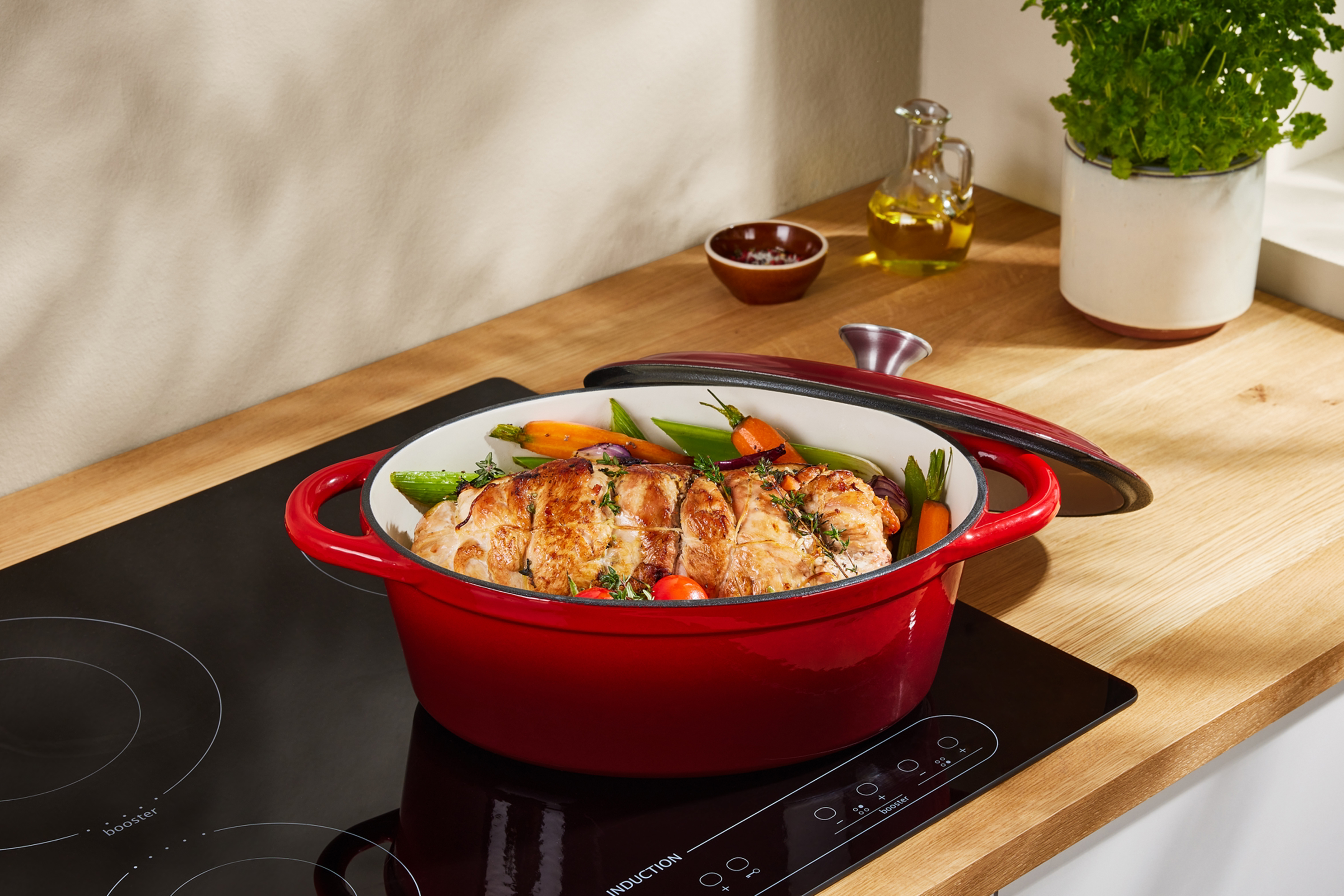 Sarkans čuguna katls ar ceptu gaļu un dārzeņiem uz indukcijas plīts virsmas.