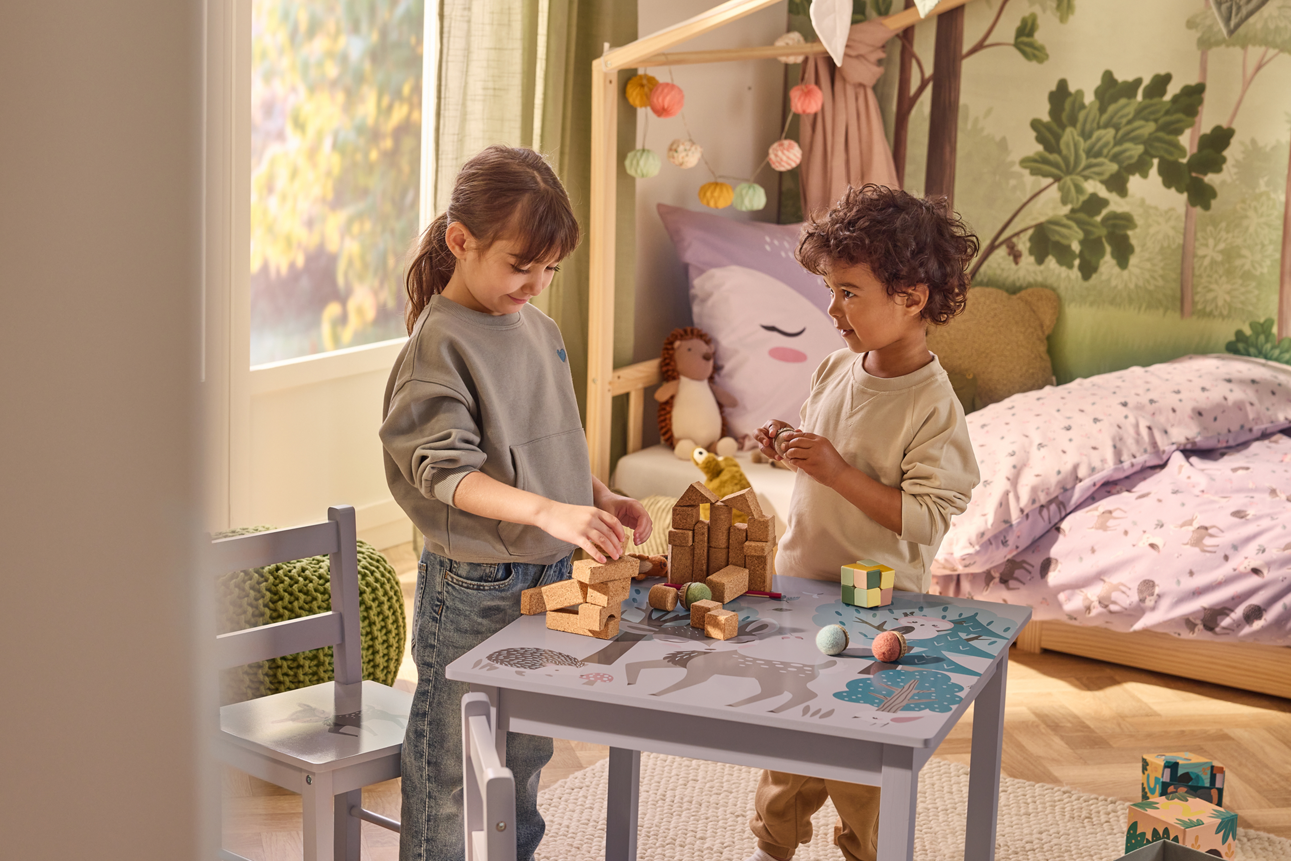 Divi bērni spēlējas ar koka klučiem pie galda bērnistabā.