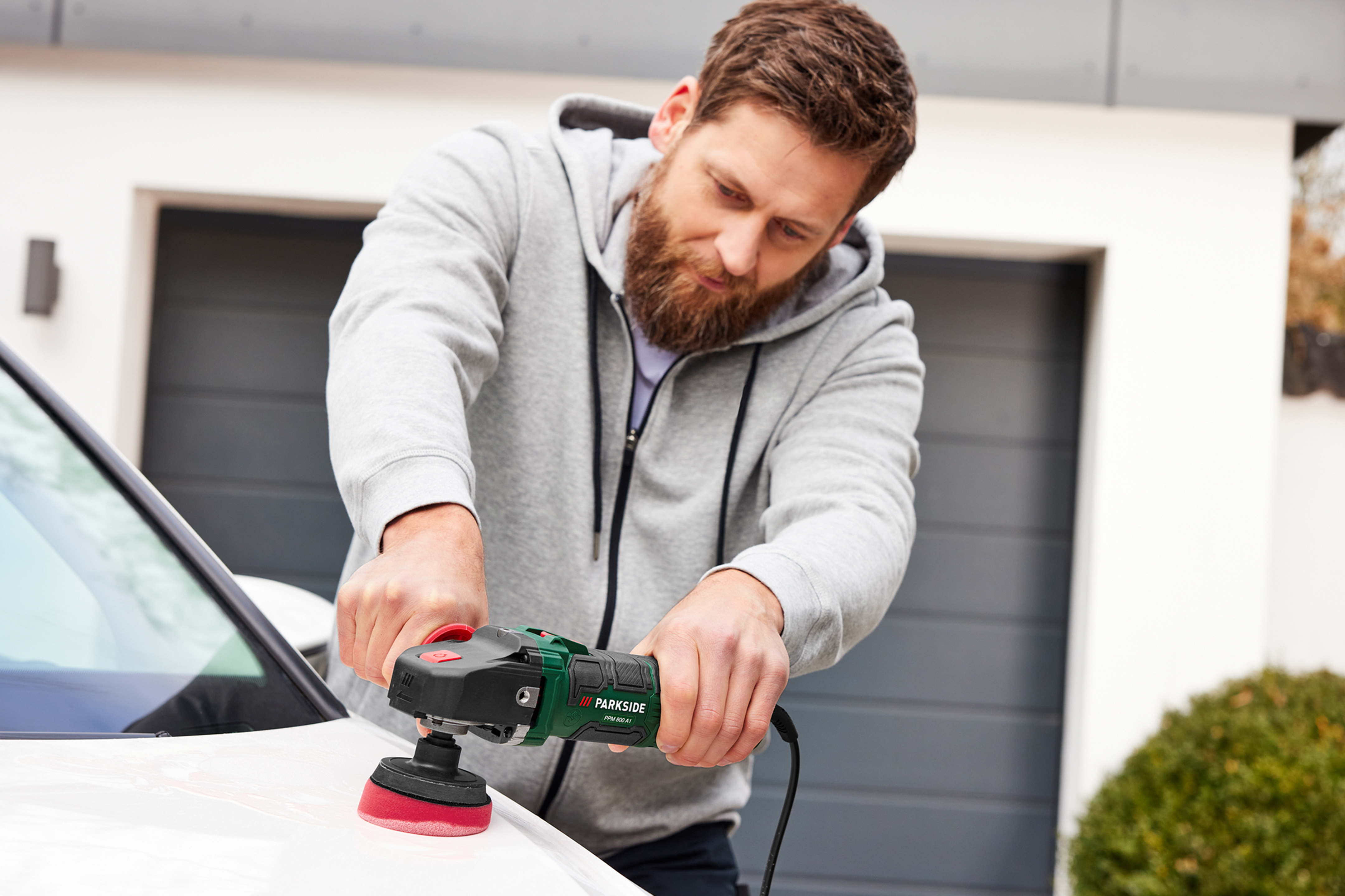 Мужчина полирует белую машину с помощью полировальной машины Parkside.