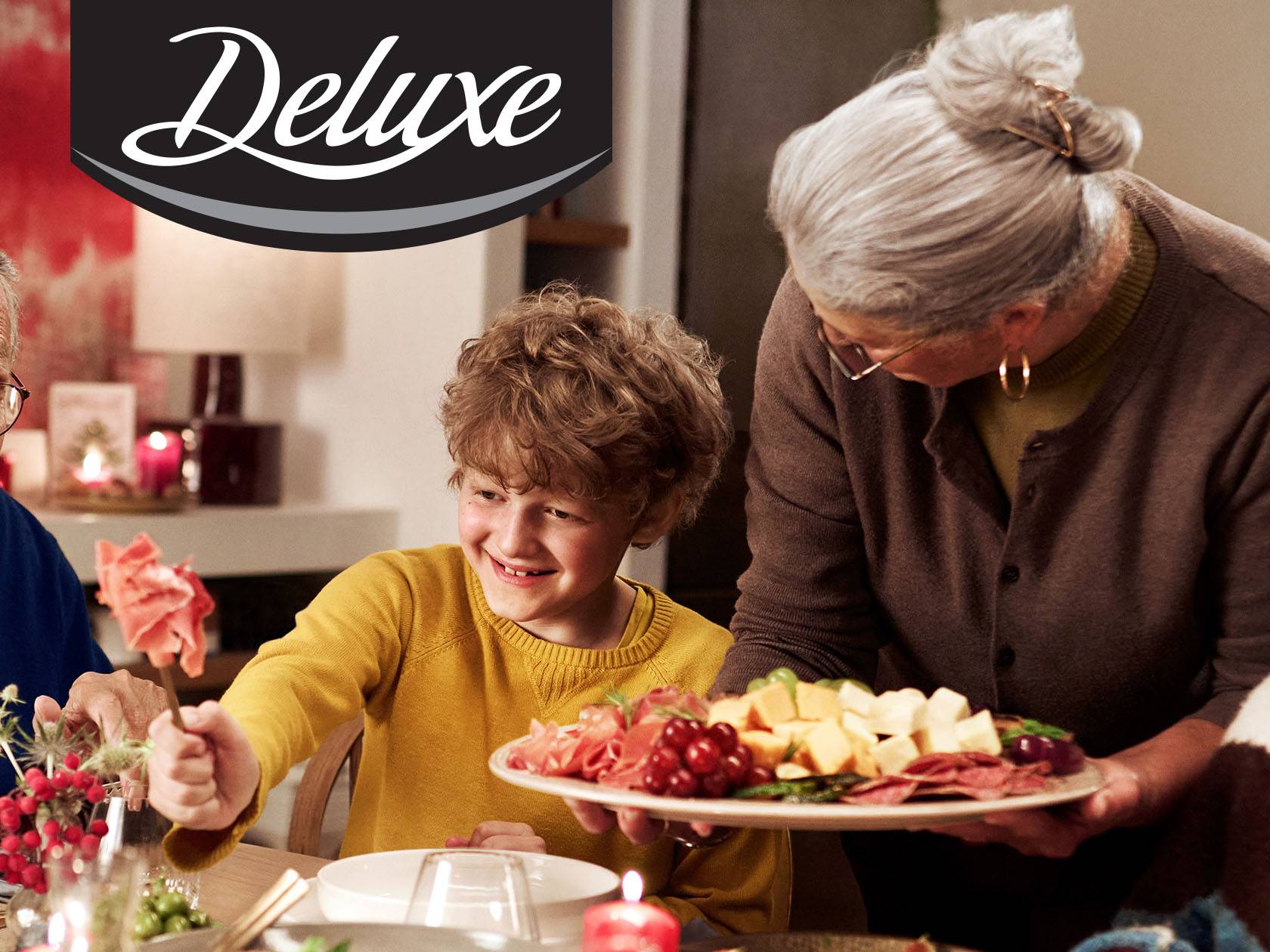 Делюкс мясная тарелка с сырами, мясом и виноградом, подаваемая женщиной улыбающемуся мальчику.