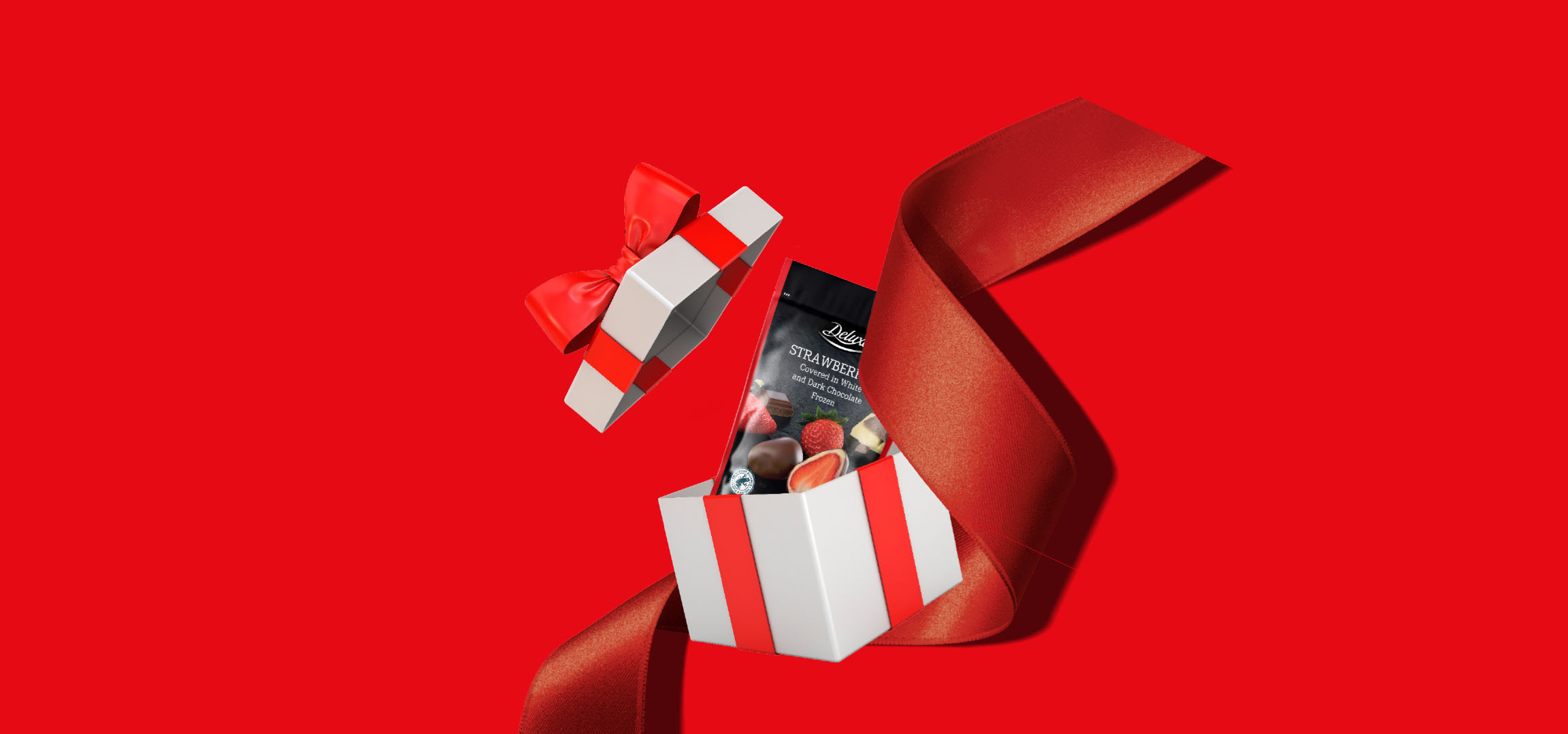 Dāvanu kastīte ar Delux šokolādes zemenēm uz sarkana fona.