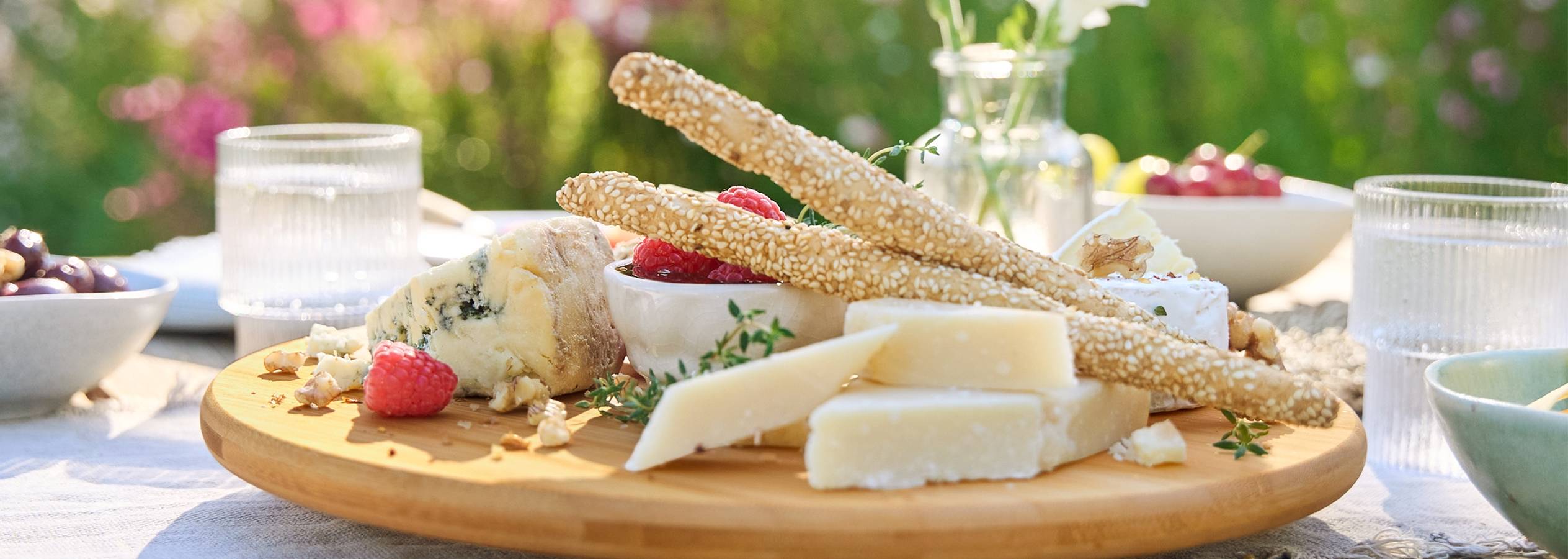 Сырная тарелка с различными сортами сыра, крекерами и ягодами на деревянной подставке.