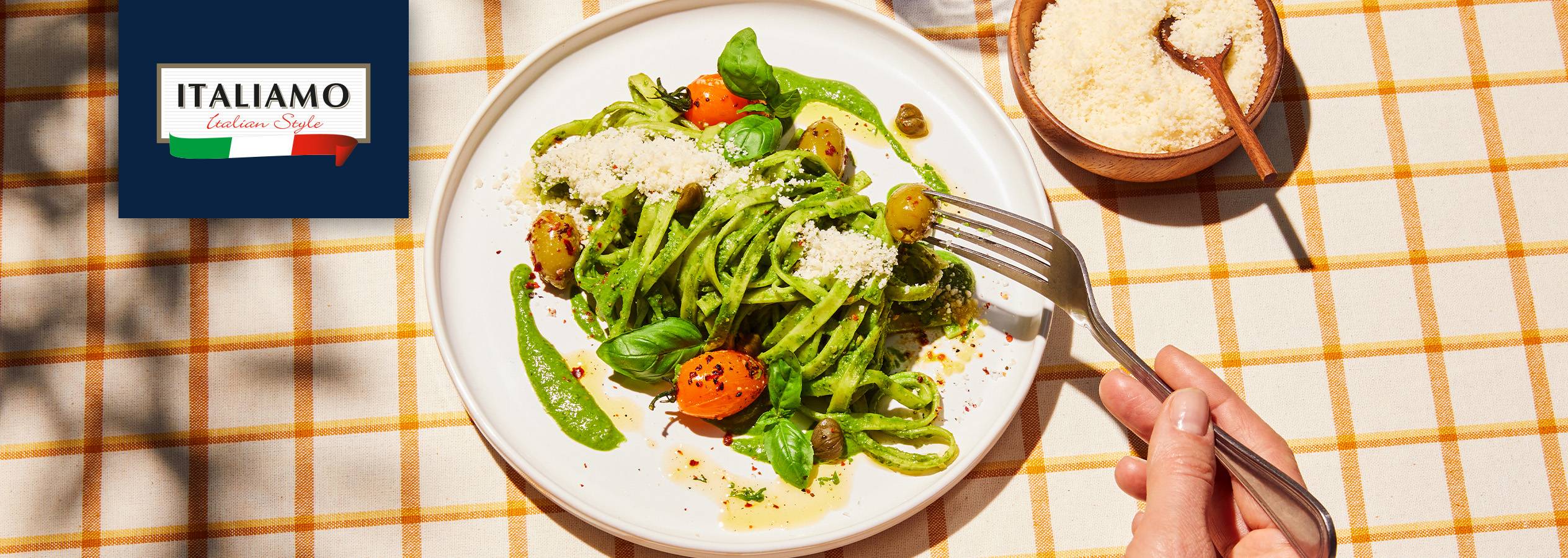 Italiamo zīmola pesto pasta ar tomātiem, olīvām un sieru uz rūtaina galdauta.