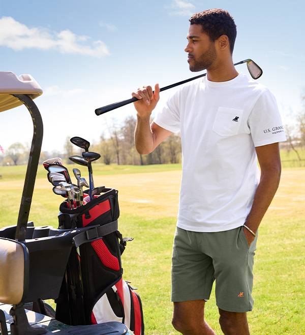 Vīrietis golfā U.S. Grand tērpā ar golfa nūjām un ratiņiem.